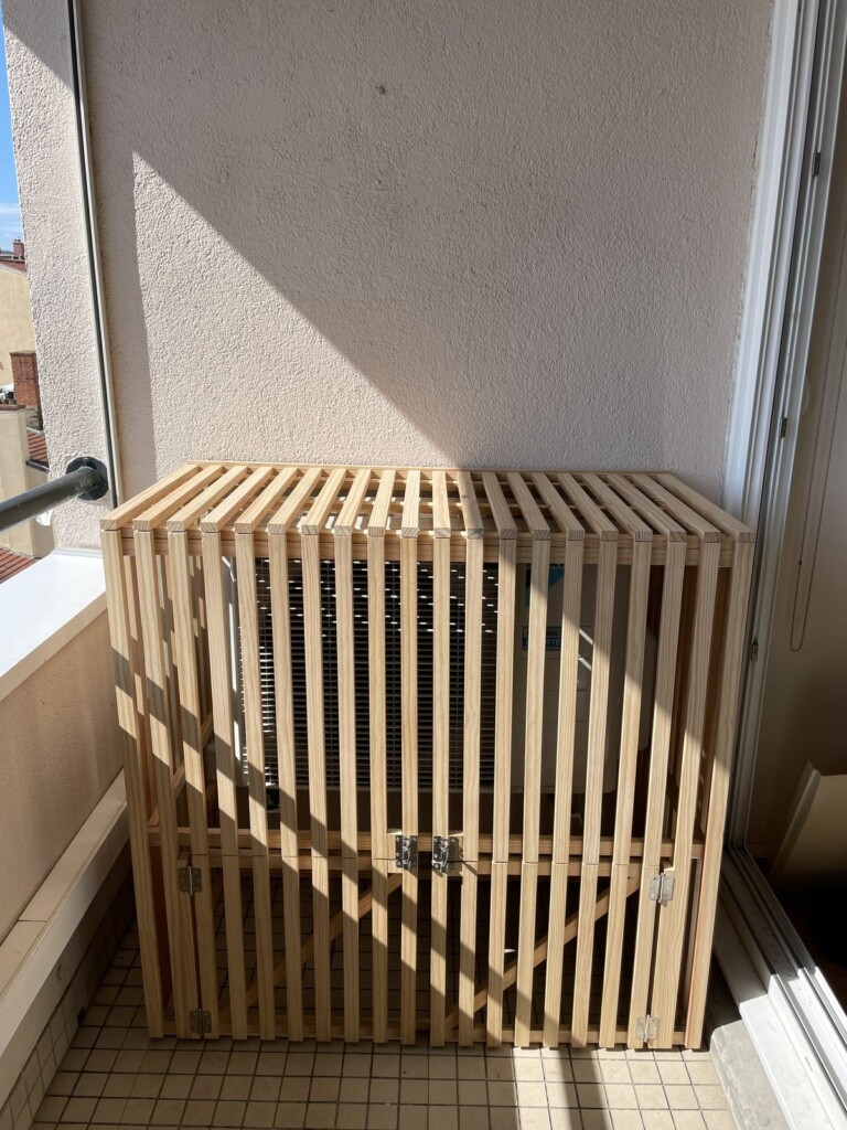 Cache ajouré sur-mesure en pin du Nord recouvrant le bloc de climatisation sur un balcon à Lyon 7, après
