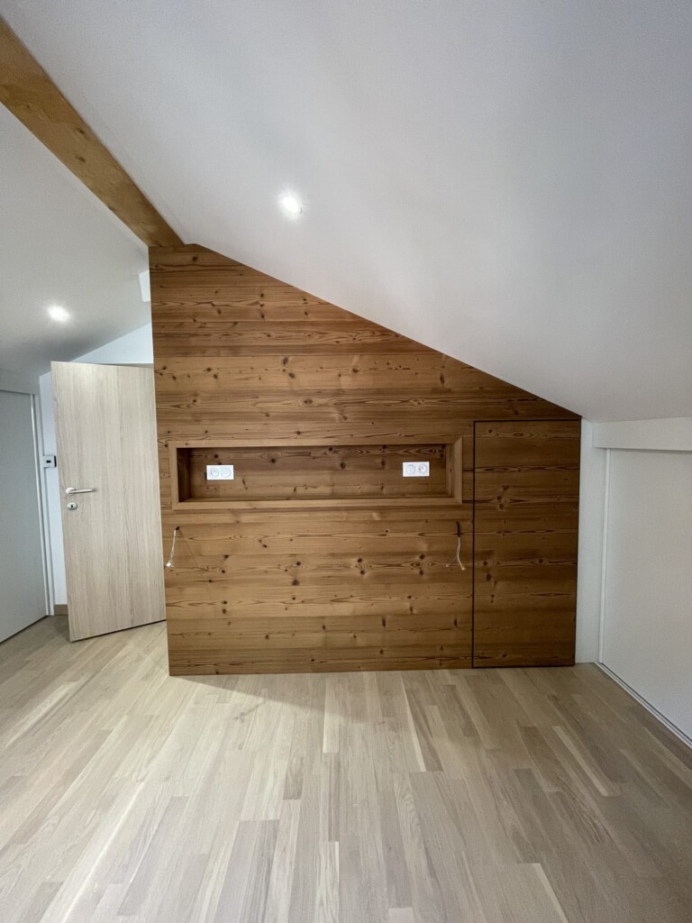 Mur sous pente habillé de bois avec porte invisible vers un placard de rangement, après